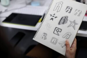 Bocetos de diseño de logotipos dibujados a mano en un cuaderno, representando el proceso creativo y la diferencia entre marca y logotipo